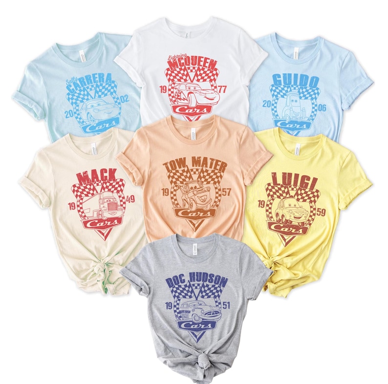 以下が含まれることがあります： 映画「カーズ」をテーマにした、異なるキャラクターが描かれた6枚のTシャツのセット。Tシャツは、薄い青、白、桃色、ベージュ、黄色、グレーなど、さまざまな色があります。各Tシャツには、キャラクターの名前と番号が書かれた市松模様のデザインが施されています。