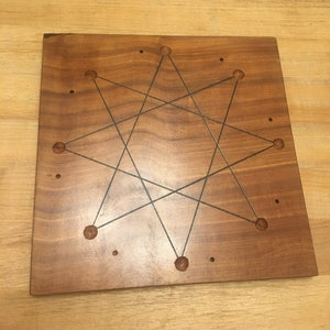 May include: A wooden game board with nine holes and lines connecting them, forming a star shape. The board is made of dark wood with a natural finish.