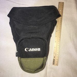 May include: Black camera bag with a green bottom and the word "Canon" printed in white on the front.