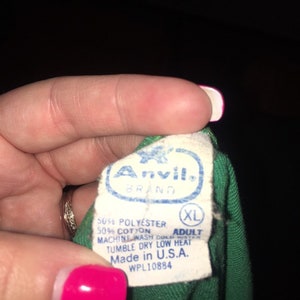 May include: A green t-shirt tag with the Anvil brand name and logo. The tag also includes the size XL, fabric content, care instructions, and "Made in U.S.A." with the WPL number 10884.