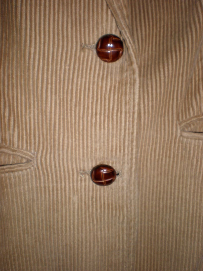 May include: Close-up of a brown corduroy jacket with two brown buttons. The buttons have a cross-hatch pattern.