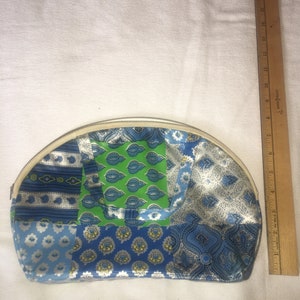 Op de afbeelding: Een halfronde blauwe en groene patchwork stoffen toilettas met een witte rits.