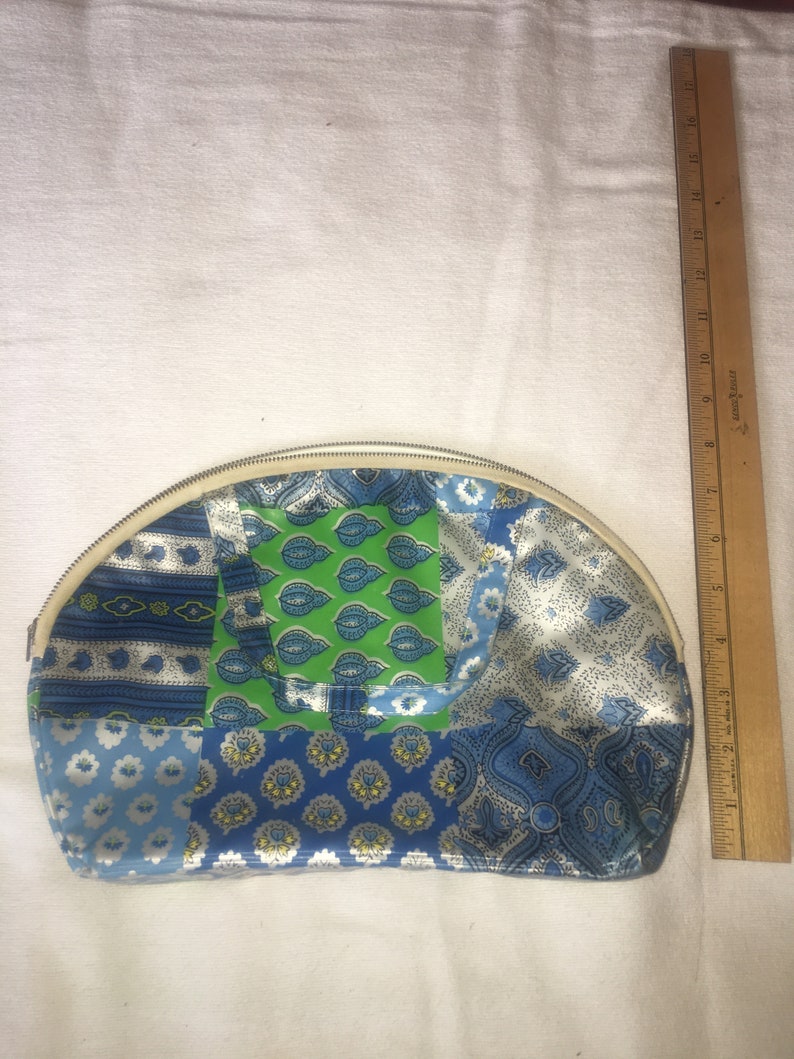Op de afbeelding: Een halfronde blauwe en groene patchwork stoffen toilettas met een witte rits.