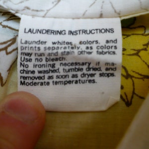 Puede incluir: Etiqueta de cuidado de la ropa blanca con texto negro que dice "Instrucciones de lavado" y proporciona instrucciones para lavar, secar y planchar. La etiqueta est&aacute; unida a una tela blanca con un estampado floral amarillo.