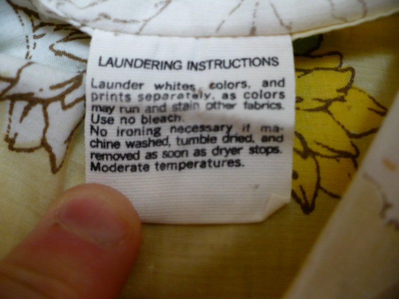 Puede incluir: Etiqueta de cuidado de la ropa blanca con texto negro que dice "Instrucciones de lavado" y proporciona instrucciones para lavar, secar y planchar. La etiqueta est&aacute; unida a una tela blanca con un estampado floral amarillo.