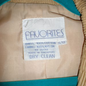 May include: A white tag with blue text that reads "FAVORITES" and details the fabric composition of the garment. The tag says "SHELL: 100% COTTON 11/12 LINING: 100% NYLON RN 35546 MADE IN SINGAPORE DRY CLEAN".