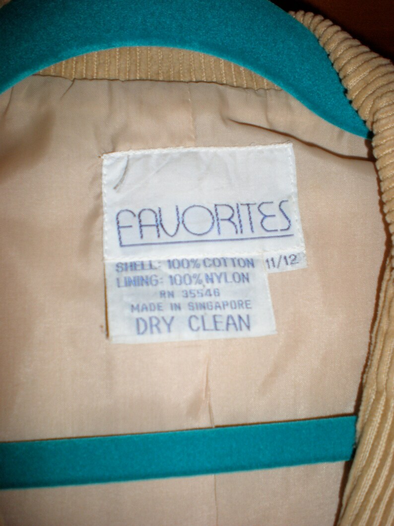 May include: A white tag with blue text that reads "FAVORITES" and details the fabric composition of the garment. The tag says "SHELL: 100% COTTON 11/12 LINING: 100% NYLON RN 35546 MADE IN SINGAPORE DRY CLEAN".