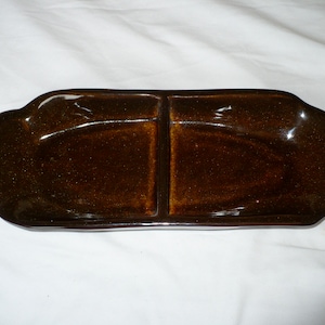May include: A brown ceramic divided serving dish with two oval-shaped compartments. The dish has a glossy finish and is perfect for serving snacks or appetizers.