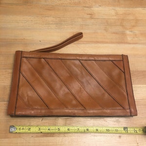 May include: A brown leather clutch with a diagonal stitched pattern and a brown leather strap. The clutch measures 30.5 cm in length.