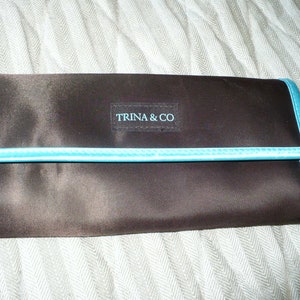May include: A brown fabric clutch with a turquoise trim and the text "TRINA & CO" in a white rectangle.
