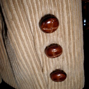 May include: Beige corduroy fabric with three brown leather buttons. The buttons are round and have a textured surface.