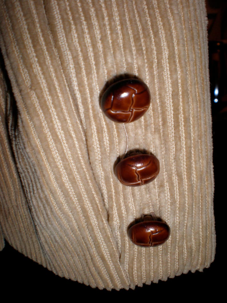 May include: Beige corduroy fabric with three brown leather buttons. The buttons are round and have a textured surface.