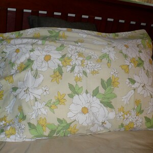 Puede incluir: Una almohada con un patr&oacute;n floral que presenta flores blancas con centros amarillos sobre un fondo beige claro. Las flores est&aacute;n rodeadas de hojas verdes.