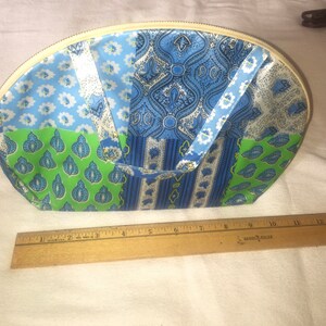 Op de afbeelding: Een wit, blauw en groen patchwork stoffen toilettas met een ritssluiting. De tas is halfrond en heeft twee stoffen handvatten.