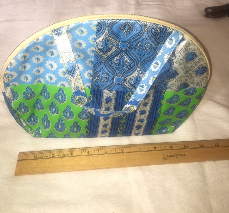 Op de afbeelding: Een wit, blauw en groen patchwork stoffen toilettas met een ritssluiting. De tas is halfrond en heeft twee stoffen handvatten.