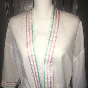 May include: White robe with a long, V-shaped neckline and a tie belt. The robe has colorful stripes along the edges of the neckline and sleeves.