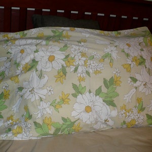 Puede incluir: Una almohada con un patr&oacute;n floral con flores blancas y hojas verdes sobre un fondo amarillo claro.