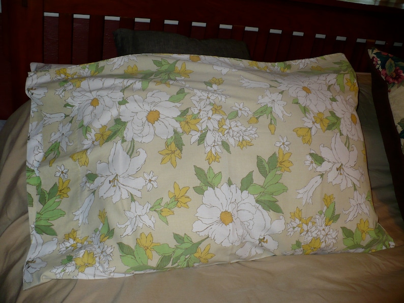 Puede incluir: Una almohada con un patr&oacute;n floral con flores blancas y hojas verdes sobre un fondo amarillo claro.