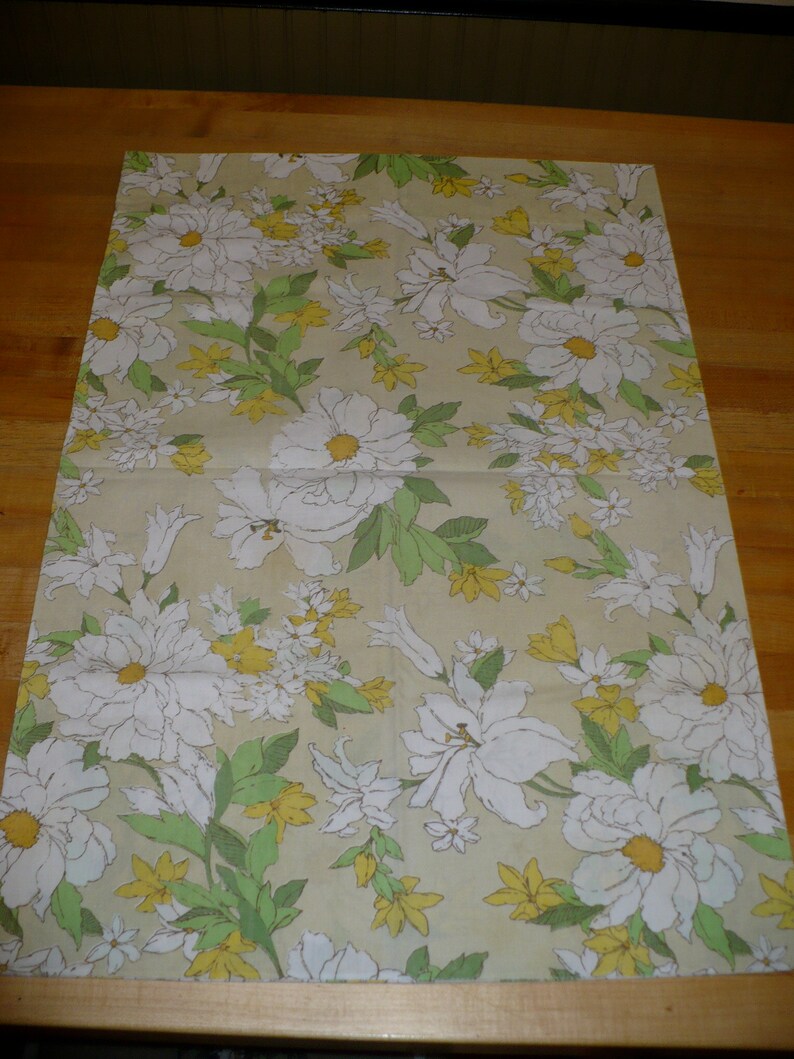 Puede incluir: Una hoja de papel de regalo beige con un patr&oacute;n floral. El patr&oacute;n presenta flores blancas con hojas verdes sobre un fondo beige.