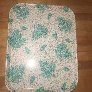 May include: A white metal serving tray with a teal leaf pattern. The tray has a speckled background.