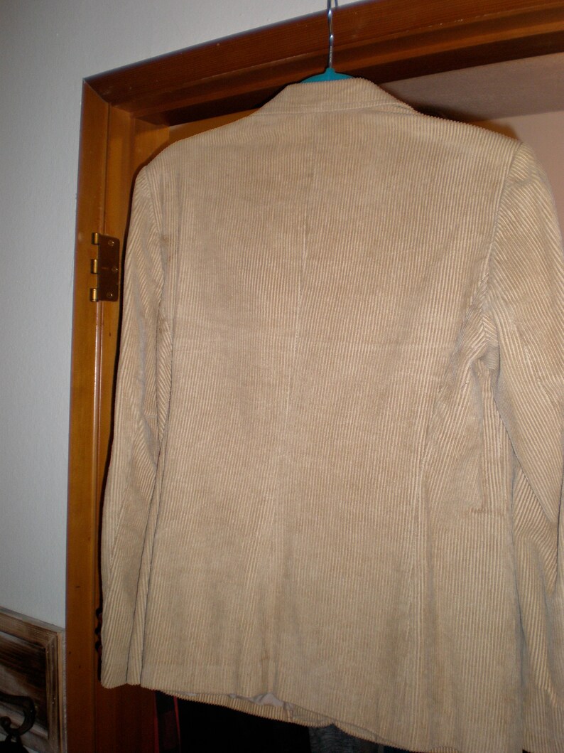 May include: A tan corduroy blazer hanging on a wooden door.