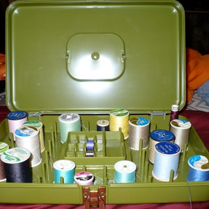 May include: A green plastic storage box with a hinged lid, filled with spools of colourful thread. The box has a compartment for storing small items.