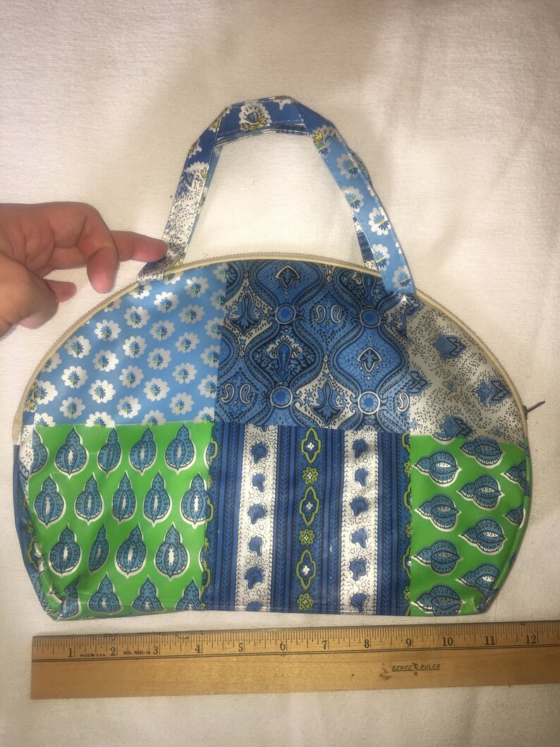 Op de afbeelding: Een blauwe en groene patchwork stoffen toilettas met een ritssluiting en een bovenste handvat. De tas is ongeveer 20 cm breed.