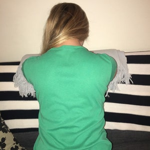 May include: A woman wearing a green t-shirt with a white fringe trim on the sleeves. She is sitting on a striped couch with a black and white pattern.