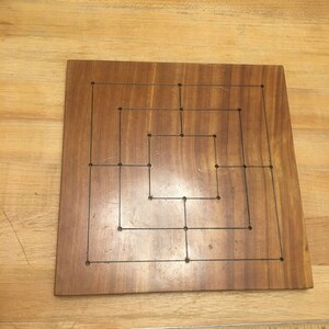 May include: A wooden game board with a grid pattern and holes for playing a game. The board is brown and has a natural wood finish.