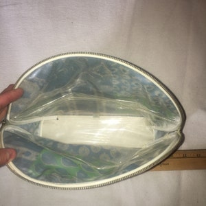 Op de afbeelding: Een doorzichtige, met een rits afsluitbare tas met een blauw en groen bloemenpatroon. De tas is open en leeg.