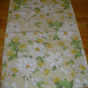 Puede incluir: Una tela beige con un patr&oacute;n floral que presenta flores blancas con centros amarillos y hojas verdes. Las flores est&aacute;n dispuestas en un patr&oacute;n repetitivo.