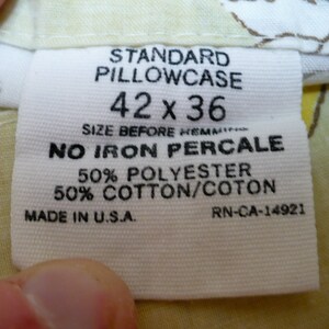 Puede incluir: Etiqueta de funda de almohada blanca con texto negro. Dice "Standard Pillowcase 42 x 36" y "No Iron Percale 50% Polyester 50% Cotton/Coton" y "Made in U.S.A. RN-CA-14921".