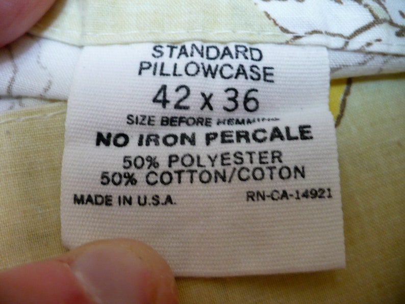 Puede incluir: Etiqueta de funda de almohada blanca con texto negro. Dice "Standard Pillowcase 42 x 36" y "No Iron Percale 50% Polyester 50% Cotton/Coton" y "Made in U.S.A. RN-CA-14921".