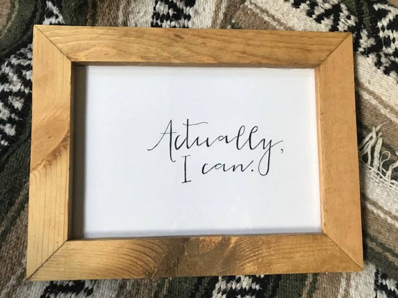 Pode incluir: Uma moldura de madeira com fundo branco e o texto "Actually, I can." escrito em caligrafia preta.