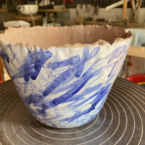 Può includere: Un vaso in ceramica bianca con un design astratto blu e bianco. Il vaso ha un bordo ruvido e testurizzato.