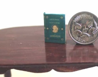 May include: A miniature green book with gold lettering and a silver coin on a dark brown oval table.