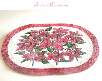 May include: Oval-shaped, red and white placemat with a printed design of red poinsettia flowers with green leaves. The placemat has a red border.