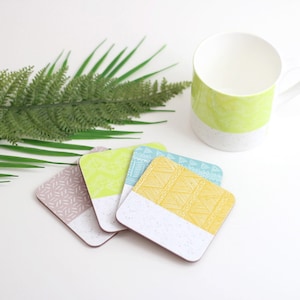 Op de afbeelding: Vier kleurrijke onderzetters met geometrische patronen. De onderzetters zijn gemaakt van kurk en hebben een witte basis. De patronen zijn geel, groen, blauw en roze.