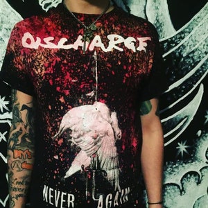 May include: A black t-shirt with a red and white splatter paint design. The shirt features the band name "DISCHARGE" and the words "NEVER AGAIN" in white lettering.