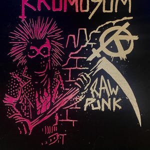 May include: Black graphic design featuring a punk figure with a mohawk, holding a scythe, and the words "Krömosom" and "Raw Punk" in pink and gold. The design includes a brick wall and an anarchy symbol.