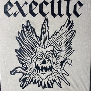May include: Cream-coloured t-shirt featuring the word "EXECUTE" in a gothic font above a black and white Medusa-style graphic. The graphic shows a skull with snakes and spiky details.