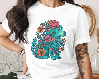 May include: White t-shirt featuring a teal dog illustration adorned with orange, pink, and teal flowers. The dog is surrounded by leaves and flowers. The design is a colorful, whimsical graphic.