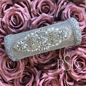 May include: A silver cylinder covered in rhinestones and pearls. The cylinder is surrounded by pink fabric roses.