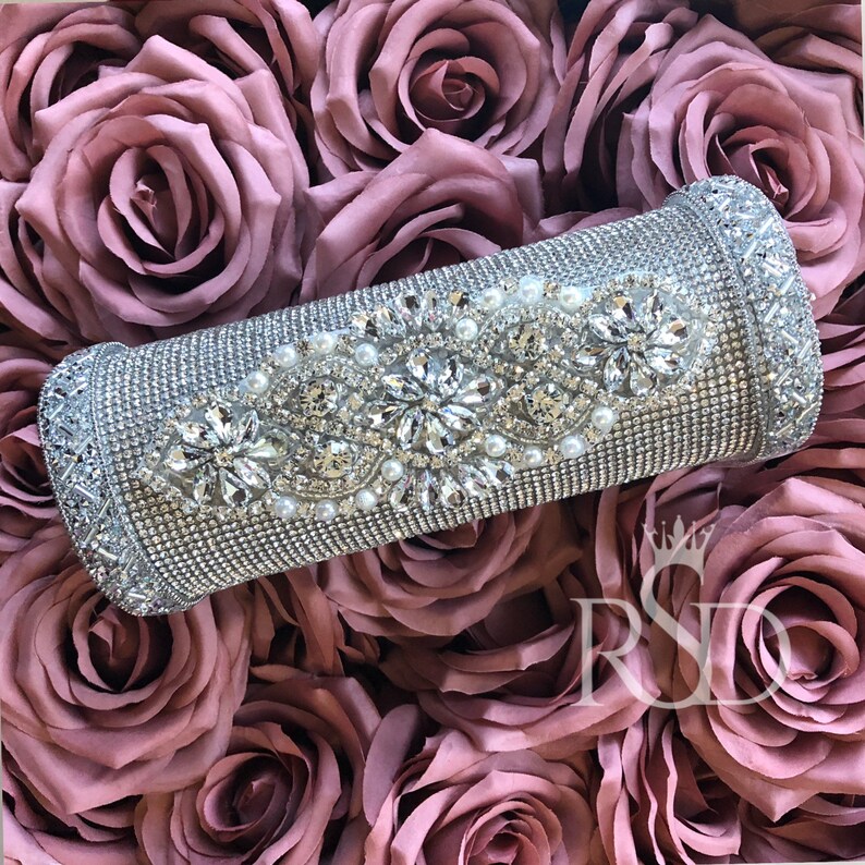May include: A silver cylinder covered in rhinestones and pearls. The cylinder is surrounded by pink fabric roses.