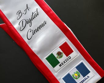 Puede incluir: Una banda de graduación blanca con rayas rojas y el texto "B.A. Digital Cinema". La banda tiene dos parches bordados, uno con la bandera mexicana y el texto "México" y el otro con la bandera guatemalteca y el texto "Guatemala".