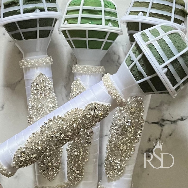 Peut inclure: Quatre supports de bouquet floraux blancs avec des inserts en mousse verte et des embellissements en strass d&eacute;coratifs.