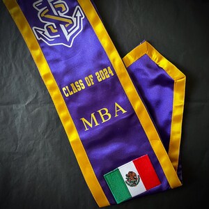 May include: Purple and gold graduation sash with the text "Class of 2024" and "MBA". A small Mexican flag is sewn onto the sash.