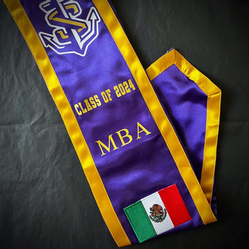 May include: Purple and gold graduation sash with the text "Class of 2024" and "MBA". A small Mexican flag is sewn onto the sash.