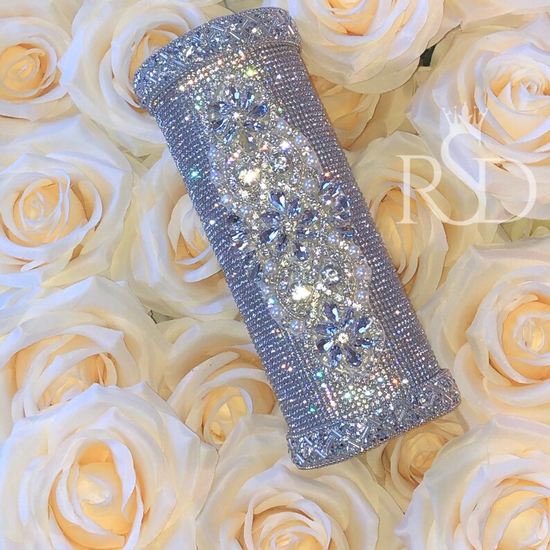 May include: A silver cylinder vase decorated with sparkling rhinestones and pearls. The vase is surrounded by white roses.