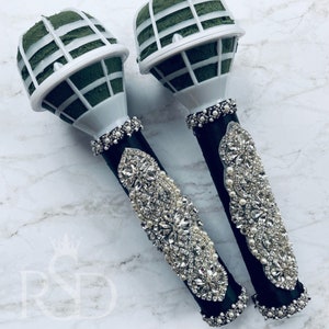 Peut inclure: Deux supports de bouquet floraux blancs et verts avec un ruban noir et des embellissements en strass. Les supports sont d&eacute;cor&eacute;s de perles blanches et de strass.